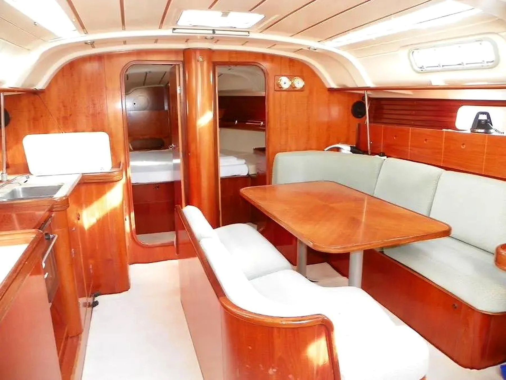 Interior compacto de barco com área de refeições, um banco e uma pequena cozinha.