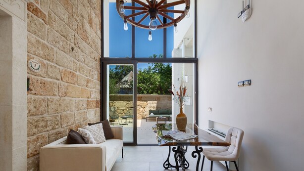 A modern interior with a stone wall, a white sofa, a glass door leading outside, and a table with chairs.
