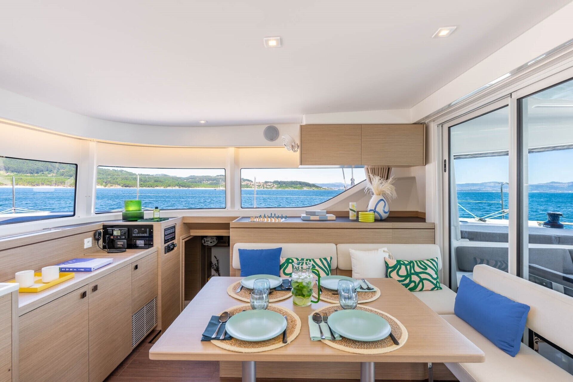 A yacht interior with a dining area, kitchen, and large windows offering sea views.