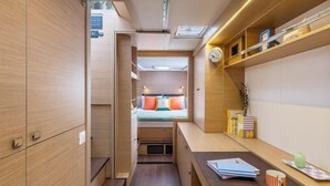 Een compact en goed verlicht interieur met een bed, bergkasten en een klein bureau.