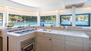 Een moderne keuken met een ingebouwde oven, een gasfornuis en een groot raam met uitzicht op zee.