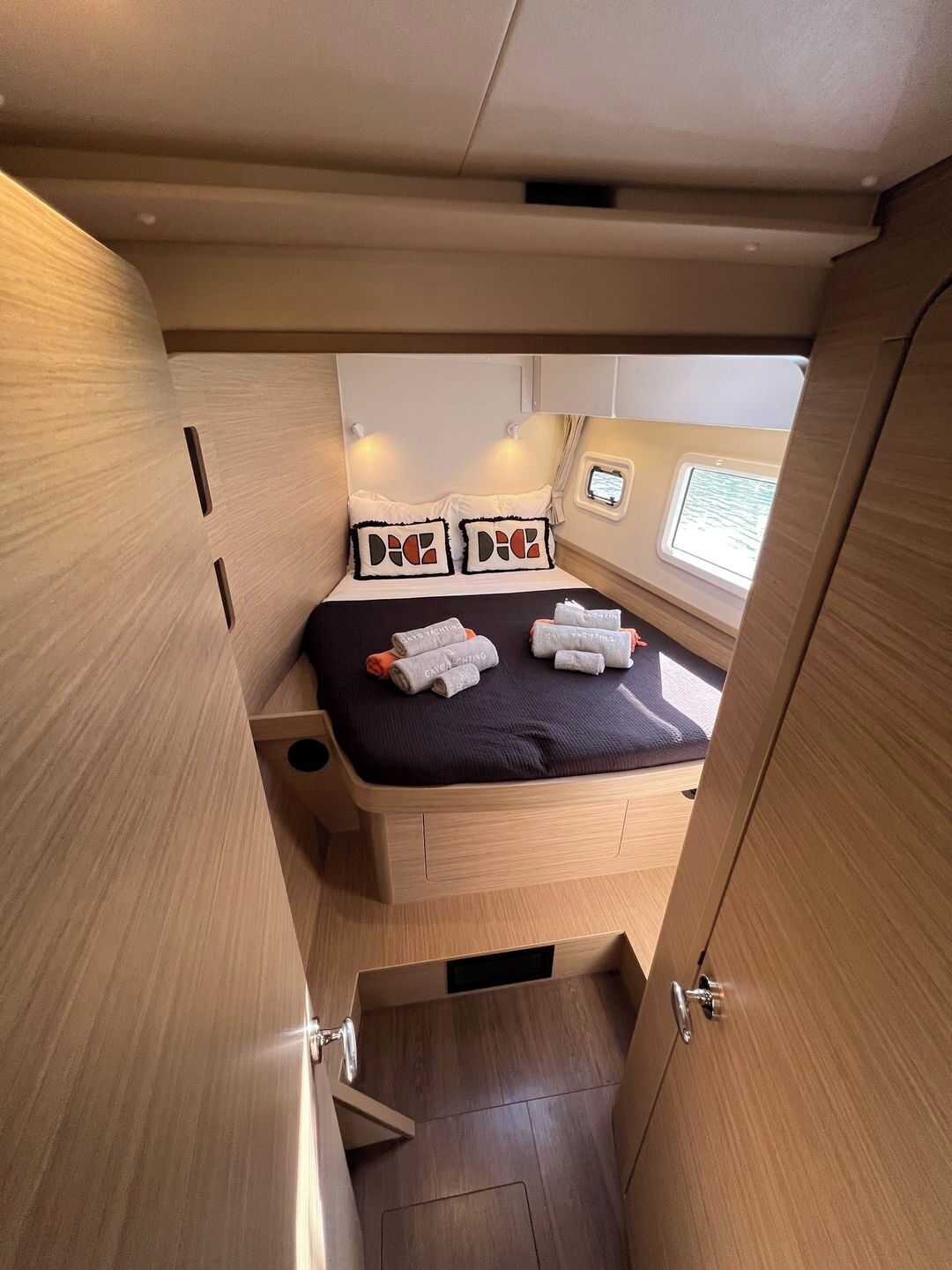 A compact, well-lit cabin with a bed, two pillows, a small window, and a built-in storage compartment.