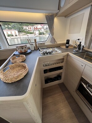 A compact kitchen with a gas stove, a sink, and a view of the water outside. - Sun-Kissed Sailing Adventure in the Ionian Islands, Lefkada (Lefkada)