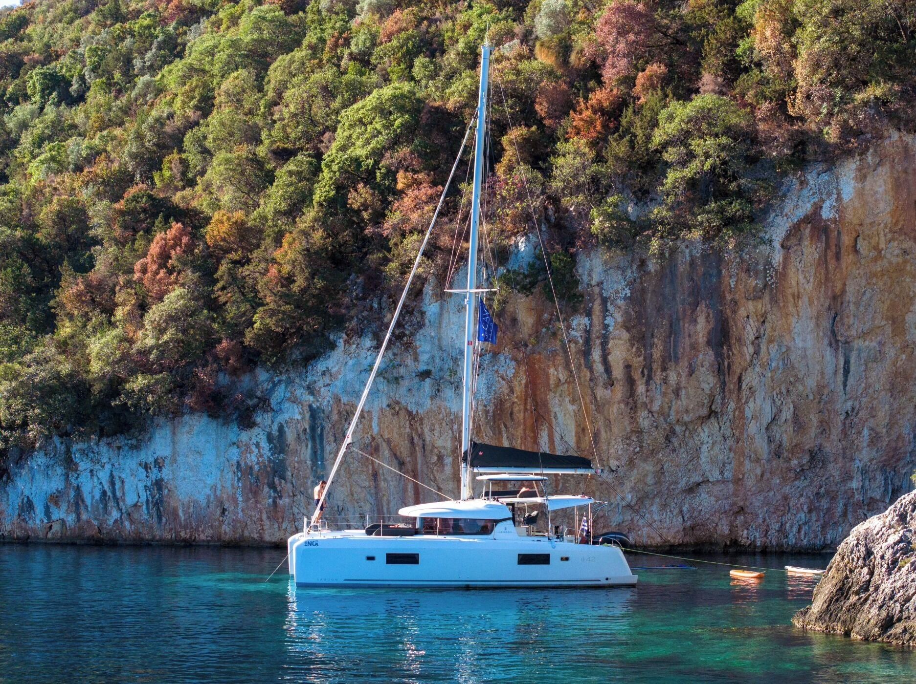 Un yacht blanc était amarré près d’une falaise rocheuse, avec une colline boisée en arrière-plan.