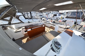 Ein Bootsdeck mit einer hölzernen Bank, einem Steuerrad und Blick auf andere Boote im Hafen.