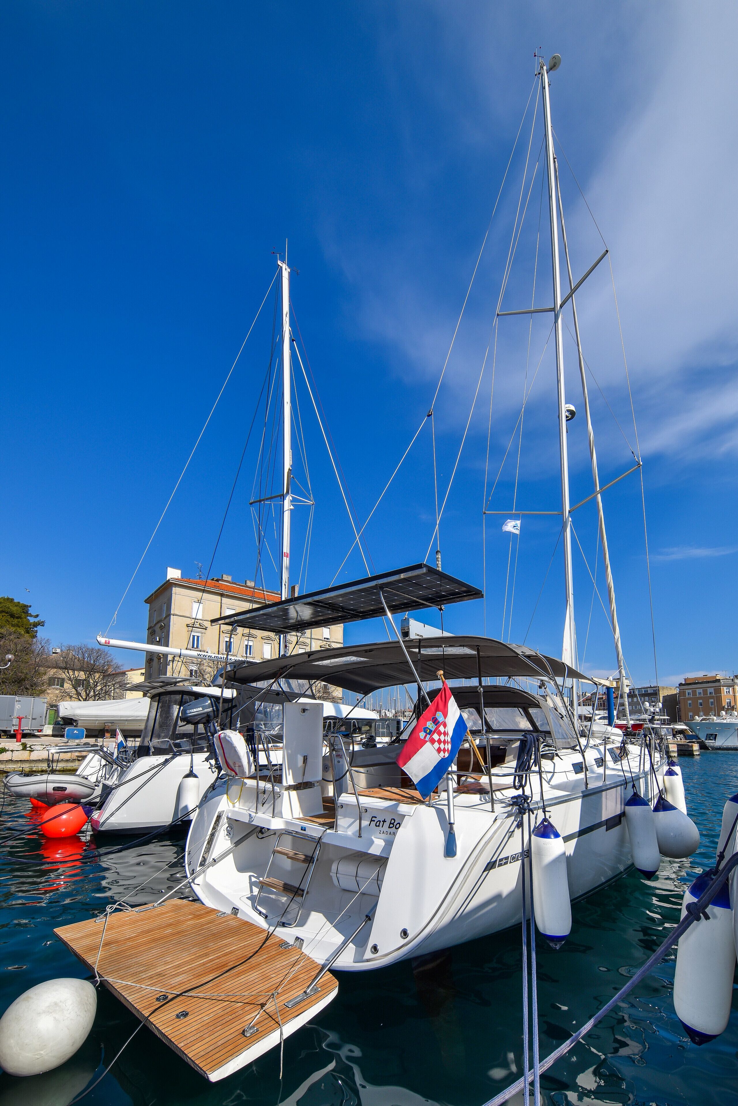 Ein Yachthafen mit mehreren Segelbooten, ein Gebäude im Hintergrund und ruhiges Wasser.