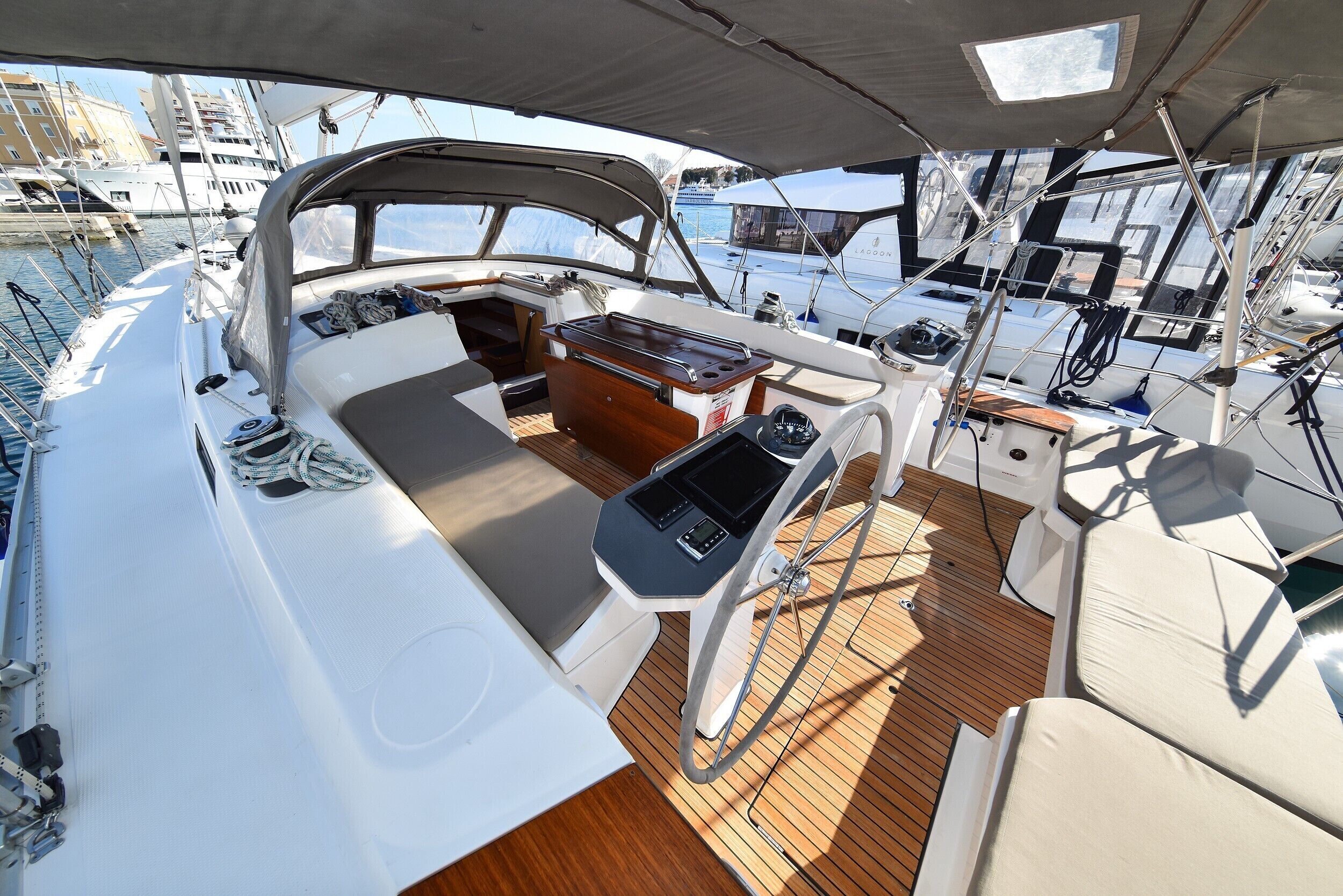 A boat deck with a wooden floor, a central seating area, and a view of other boats in the marina.