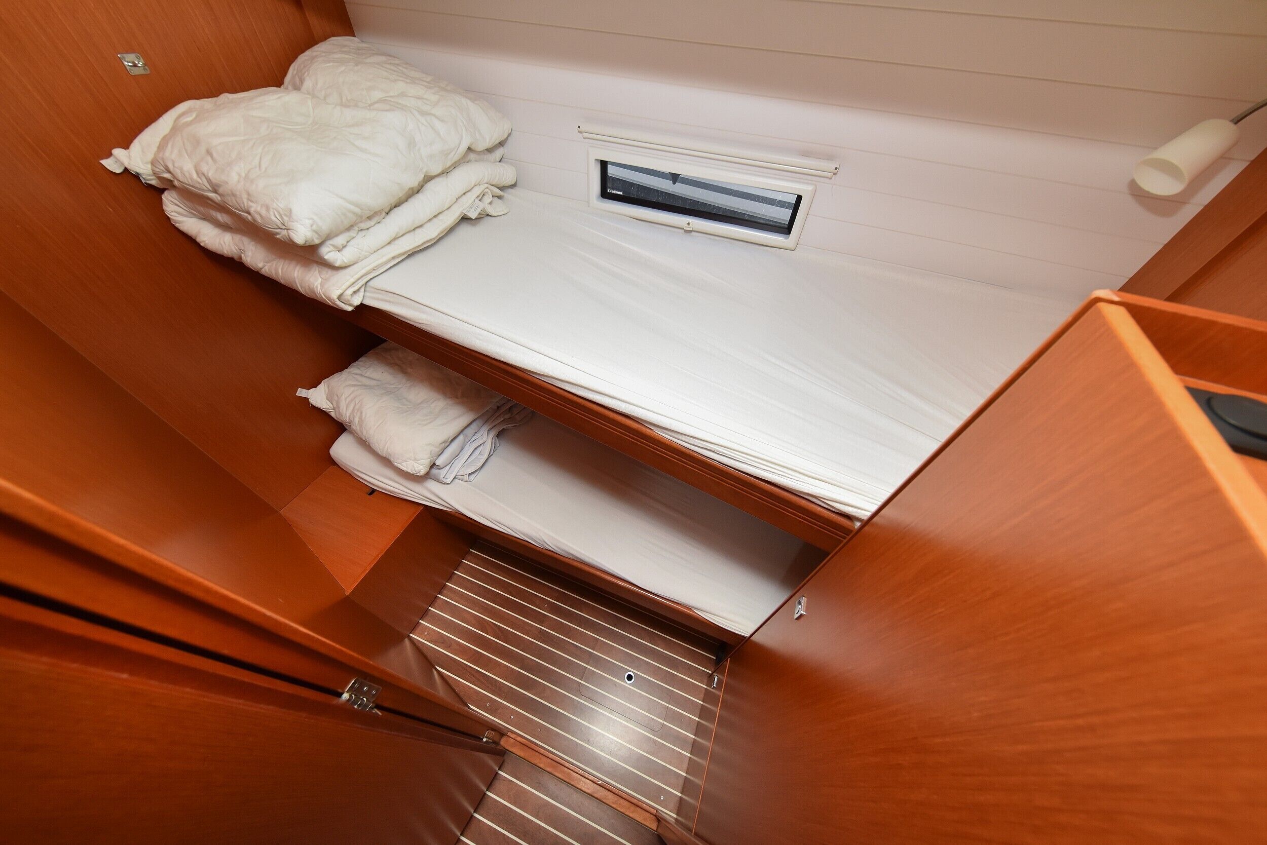 A compact room with a bunk bed, a small window, and a wooden floor.
