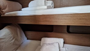 A bunk bed with white bedding and pillows, a wooden headboard, and a lower bunk with a pillow and folded towel. - Sun-Kissed Sailing Adventure in Islas Sarónicas (Alimos)