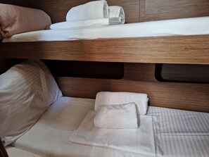Ein Etagenbett mit weißer Bettwäsche und Kissen, ein Holz-Kopfstück und eine untere Schlafstelle mit Kissen und gefaltetem Handtuch.