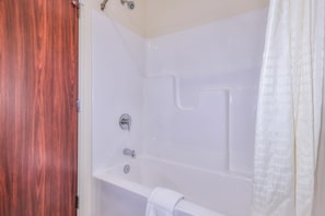 A white bathtub with a shower curtain, a towel, and a wooden door.