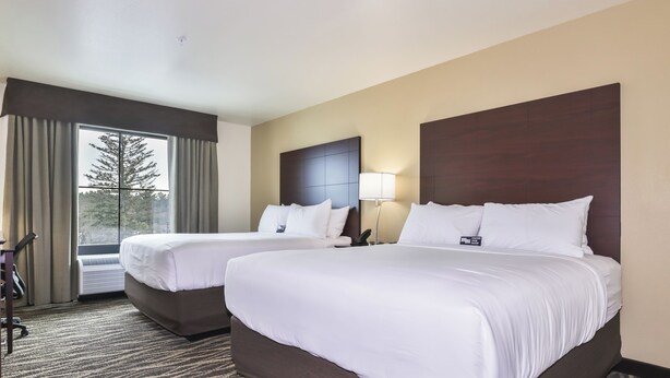 A hotel room with two beds, a large window with curtains, a wall-mounted lamp, and a carpeted floor. - Cobblestone Hotel & Suites - Montevallo (Montevallo)