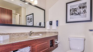 A bathroom with a granite countertop, wooden vanity, a white toilet, a large mirror, and a framed black and white photo on the wall. - Cobblestone Hotel & Suites - Montevallo (Montevallo)