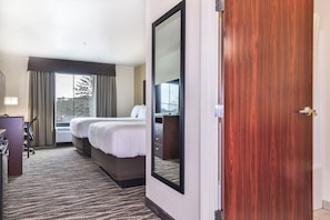 A hotel room with a large bed, a desk, a chair, a dresser, and a window with curtains.