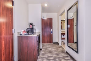 A hotel hallway with a coffee station, a wooden door, and a mirror on the wall.