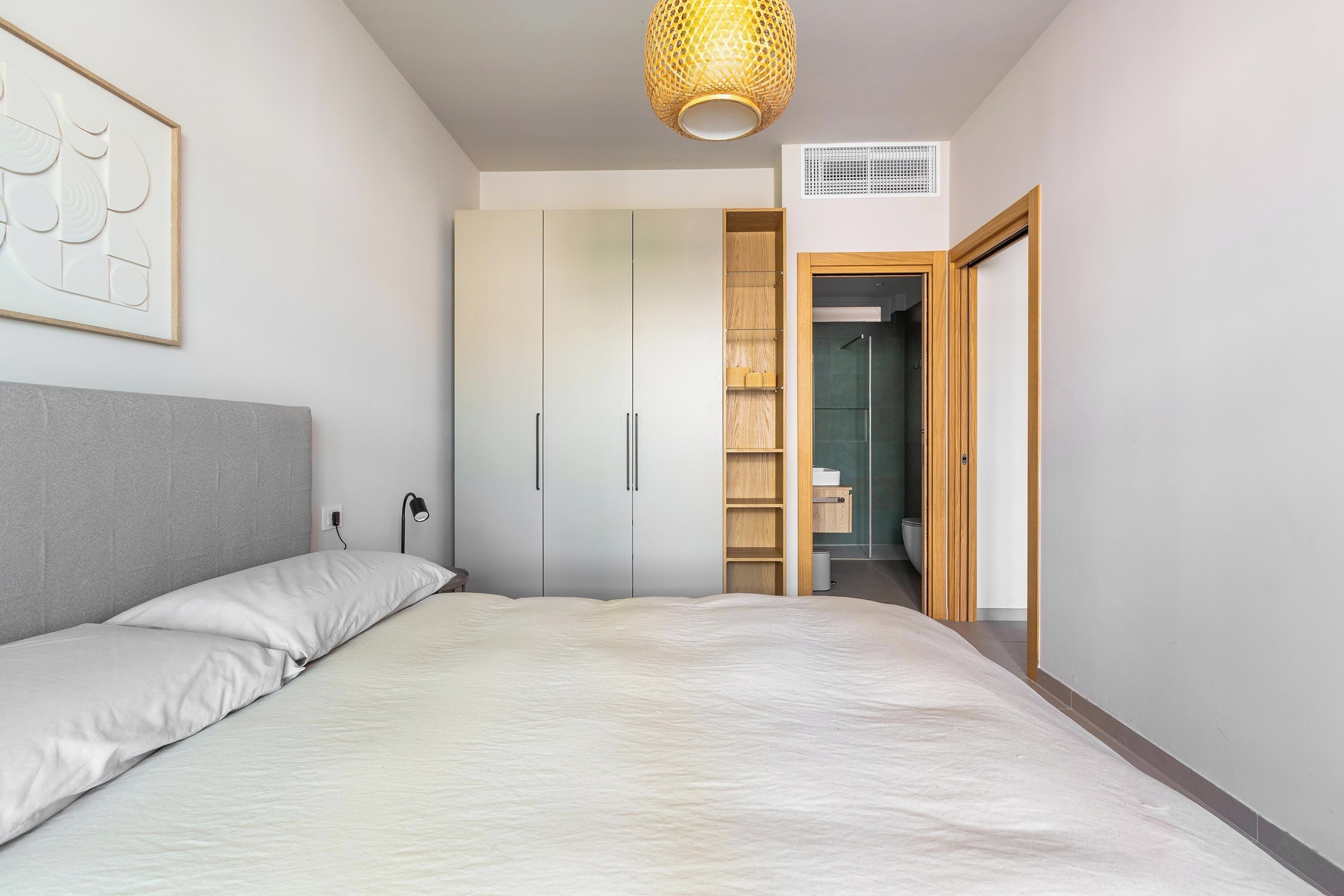 Une chambre à coucher comprenant un lit, une armoire, une table de chevet, une lampe et un luminaire suspendu.