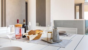 Una mesa de comedor con una botella de vino, copas, pan y una jarra de aceite.