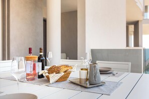 A dining table with a bottle of wine, glasses, bread, and a pitcher of oil. - Zefiro Suite by BarbarHouse (Gallipoli)