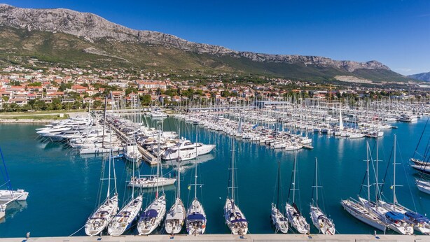 A marina with numerous boats docked, a town in the background, and mountains. - Sun-Kissed Sailing Adventure in Split, Croatia (Kaštel Gomilica)