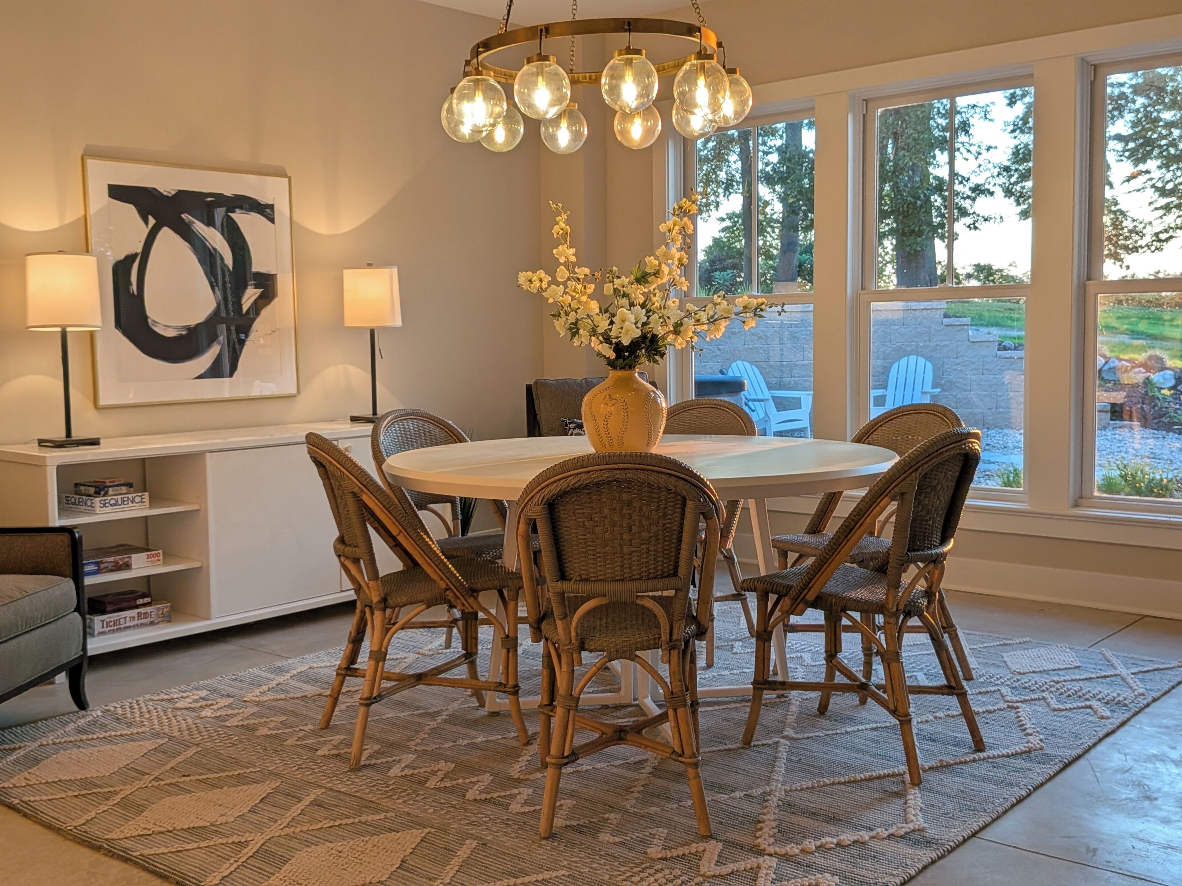 A dining area with wicker chairs, a round table, a vase with flowers, and a chandelier.