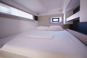 Ein Einzelbett mit ordentlich zusammengefaltetem Bettbezug, ein kleines Fenster und Einbauschränke.