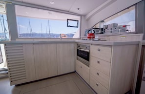 A compact kitchen with a view of the marina, a small oven, and a kettle. - Sun-Kissed Sailing Adventure in the Ionian Islands, Lefkada (Lefkada)