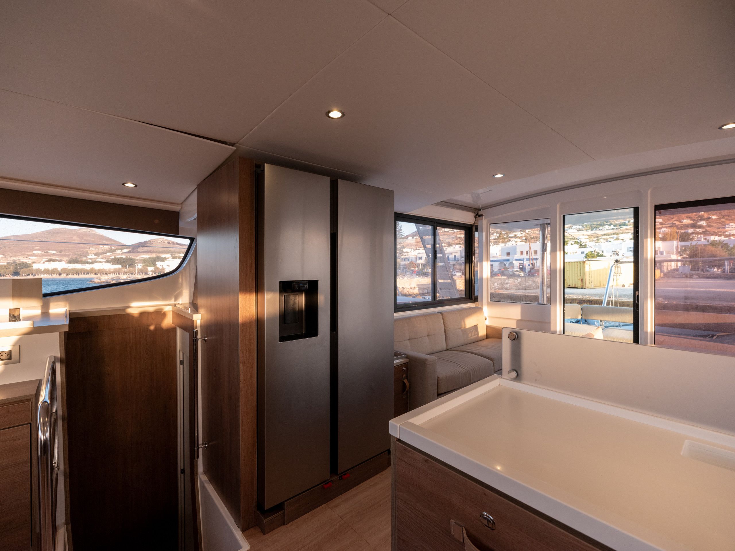 A modern kitchen with a built-in refrigerator, a seating area with a sofa, and large windows offering a view of the landscape.