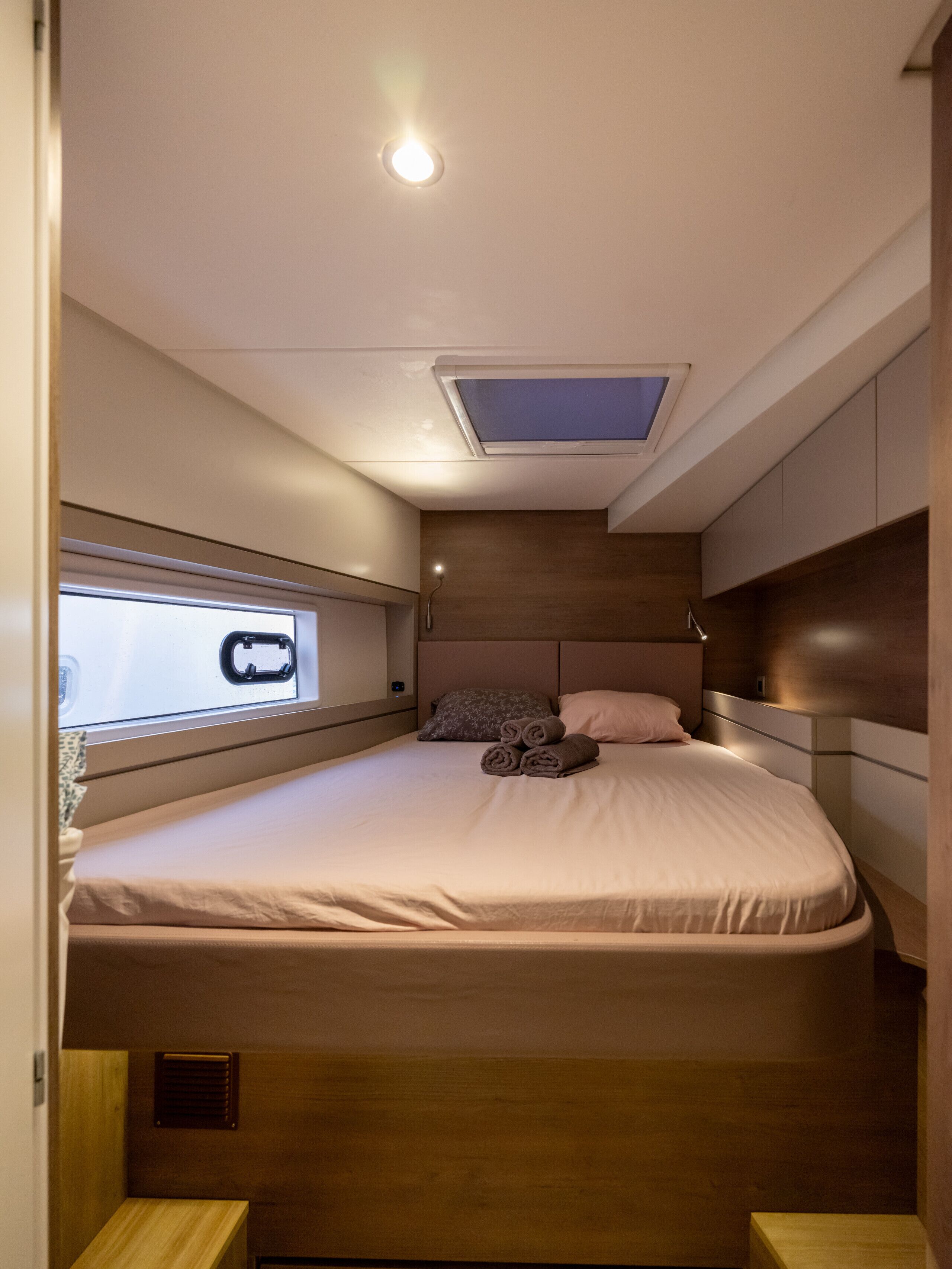 A compact bedroom with a bed, a skylight, a window, and built-in storage.