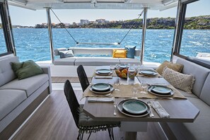 Ein Essbereich auf einem Boot mit einem Tisch für vier Personen, einer Couch und Blick aufs Meer.