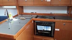 Una cuina americana petita amb un rentapeus, fogó i forn, armaris de fusta i una finestra sobre el rentapeus.