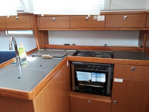 Una kitchenette compacta con pileta, hornalla y horno, muebles de madera y una ventana sobre la pileta.