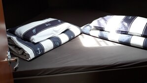 A compact, well-lit cabin with a single bed featuring navy and white bedding with anchor designs, a wooden headboard, and a small overhead storage space.