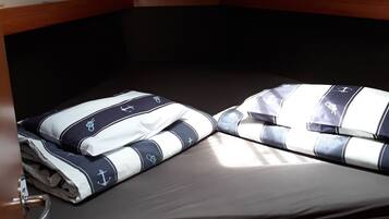 A bunk bed with navy and white bedding featuring anchor designs, a wooden headboard, and a small overhead compartment.