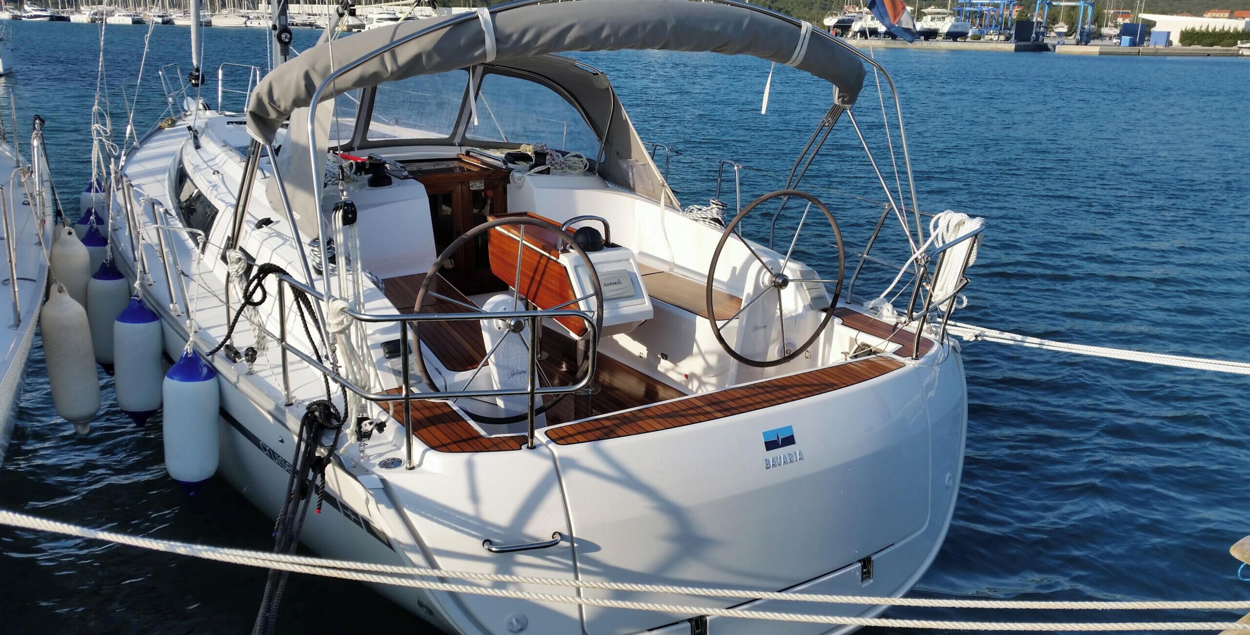 Un voilier est amarré dans une marina. On peut y voir une cabine, une roue de barre, ainsi que divers cordages et bouées.