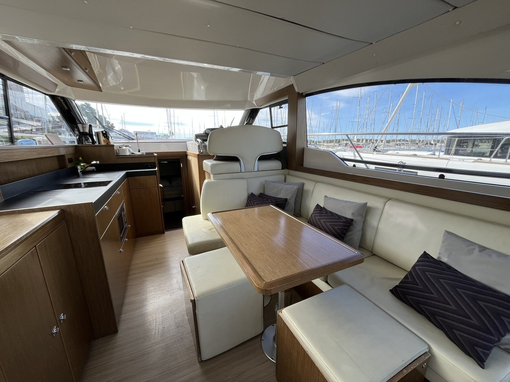 A yacht interior with a dining area, seating, and a view of the marina.