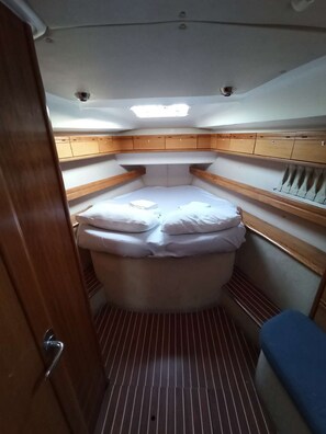 Eine kompakte Kabine auf einem Boot mit einem Schlafkoje, Stauraumschränken und einer kleinen Sitzecke.