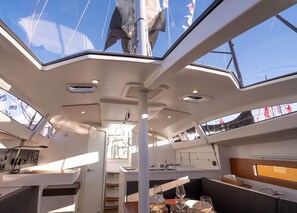 A yacht interior with a dining area, a control panel, and a view of the deck.