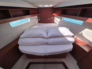 Ein kleines Bett mit weißer Bettwäsche in einer Holzhütte mit eingebauten Fenstern.