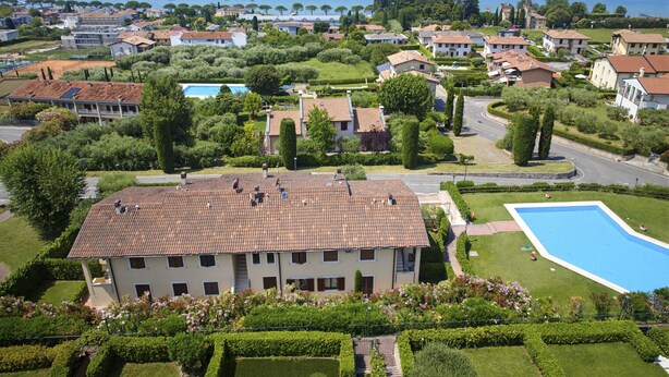 Zona residencial con un edificio grande que tiene piscina, rodeado de jardines cuidados y vistas al mar.