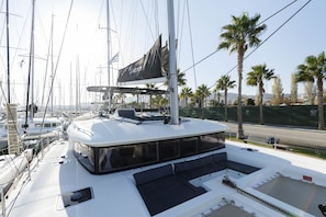 A yacht with a covered deck area, seating arrangements, and a view of the marina and palm trees. - Sun-Kissed Sailing Adventure in the Dodecanese Islands (Rodos)