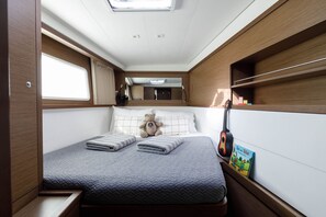 Een compact interieur van een camper met een bed, een raam, een spiegel en een klein plankje met een boek.