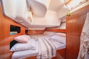 Une petite cabine équipée d’un lit superposé, de murs en bois, d’une petite étagère avec des livres et d’un luminaire suspendu.