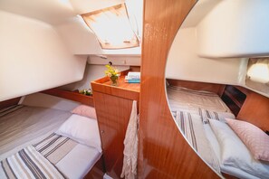A compact cabin with two berths, a small wooden table with a vase of flowers, and a book titled 'SENEK Greek Islands.'