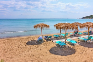 Una playa con tumbonas y sombrillas de paja, orilla arenosa y mar tranquilo.