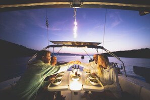 A boat with a table set for dining, surrounded by water and a sunset in the background.