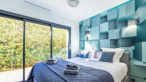 Ein modernes Schlafzimmer mit einem großen Bett, Blick ins Grüne und einem geometrischen Wanddesign.