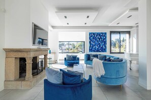 Ein modernes Wohnzimmer mit Kamin aus Naturstein, blauen Sofas und einem großen Fenster mit Blick auf die Stadt.