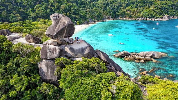 Paisagem costeira com grandes rochas, água turquesa límpida e floresta verde densa.