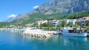 A coastal marina with boats, a rocky breakwater, and buildings with red roofs. - Sun-Kissed Sailing Adventure in Split-Dalmacia, Croatia (Tucepi)