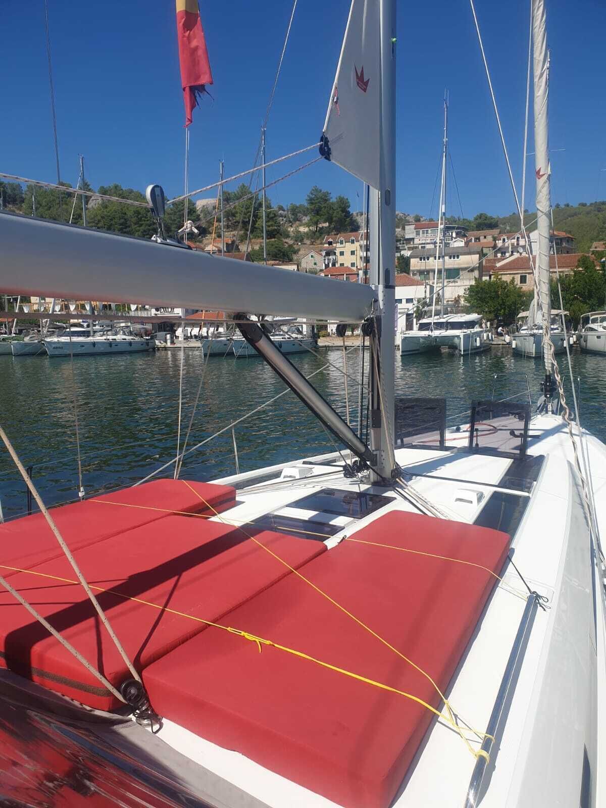 A sailboat docked at a marina with a red deck, white hull, and a clear view of the marina and buildings in the background.